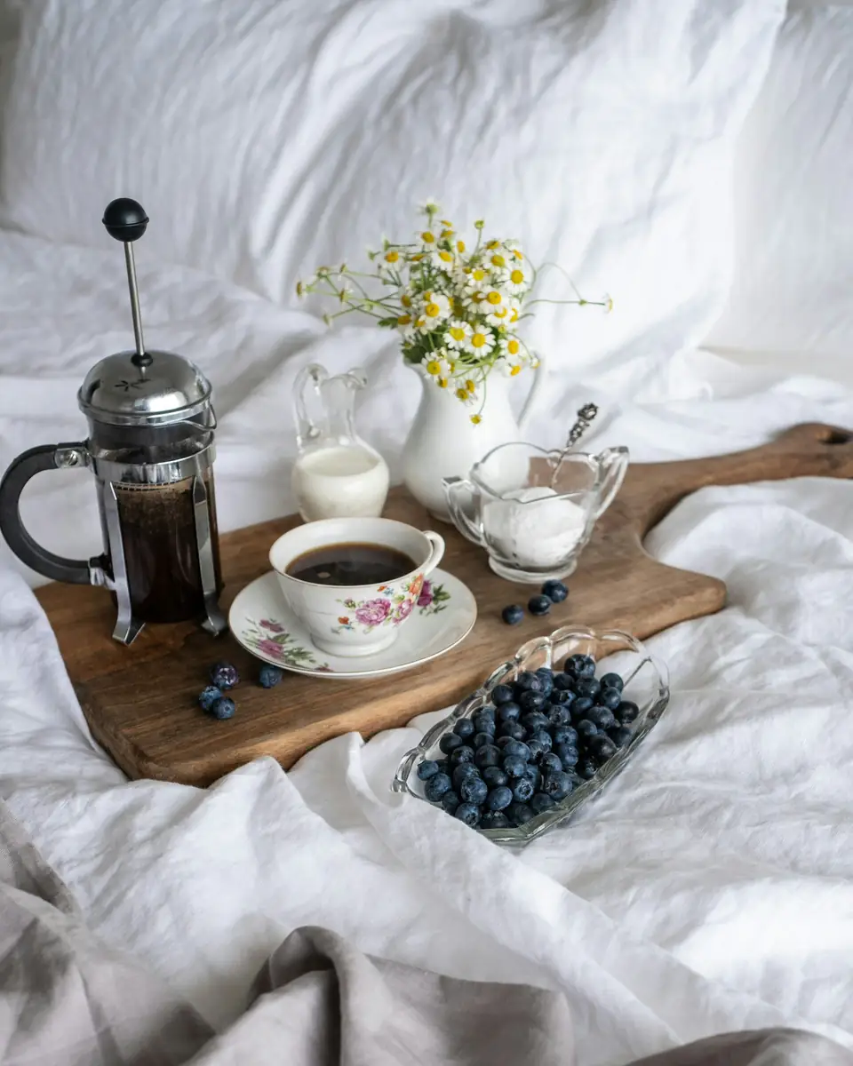 Bandeja de madera con café, arándanos y flores sobre la cama