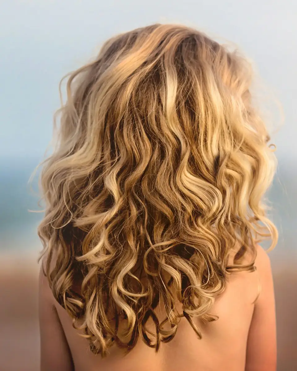 Pelo rubio en ondas sueltas, de espaldas, con el mar desenfocado