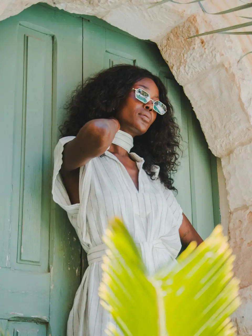 Una mujer de lentes blancos y vestido blanco posa junto a una puerta verde