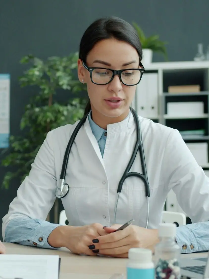 Una médica con lentes y estetoscopio atiende en su consultorio