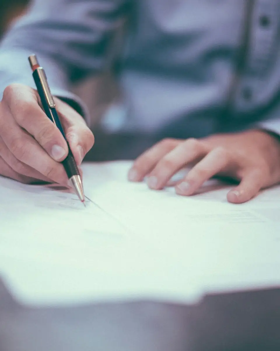 Una persona firmando documentos sobre un escritorio