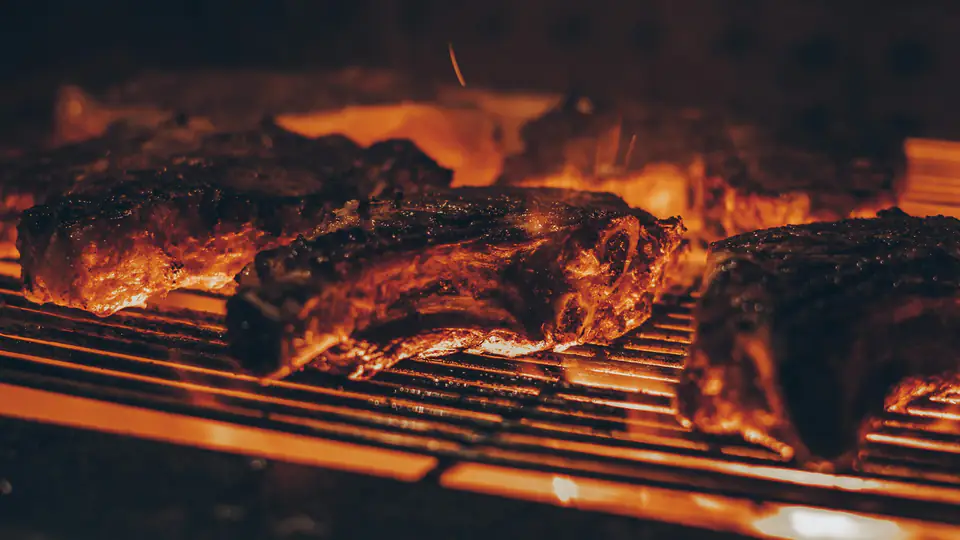 Cortes de carne dorándose sobre la parrilla, con las brasas encendidas