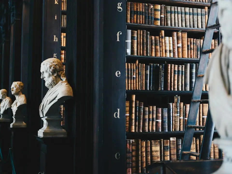 Biblioteca de madera con libros antiguos y bustos de mármol