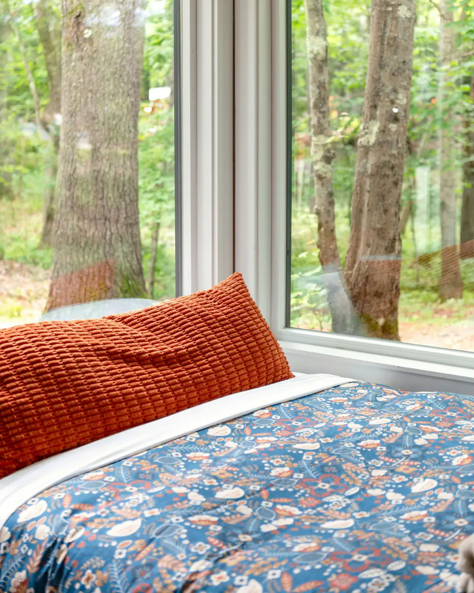 Cama con almohadón naranja junto a un ventanal
